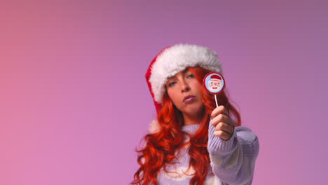 Studio-Portrait-Shot-Of-Young-Gen-Z-Woman-Wearing-Christmas-Santa-Hat-Holding-Candy-Lollipop